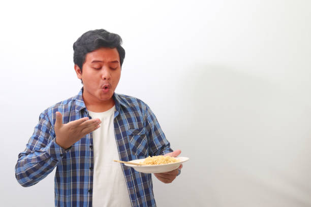 Portrait of shocked Asian man in plaid shirt eating spicy noodle and turning his face become red. Isolated image on white background