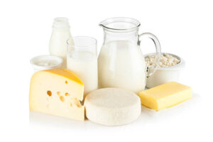 Image of dairy products shot on reflective white backdrop. Includes: milk, various types of cheese, butter, ricotta, milk cream and yogurt. A milk pitcher and a glass of milk are in the center while the rest of the products are around them. A soft shadow is visible in the foreground. The predominant color is white. dairy milk is a Foods that are difficult to digest